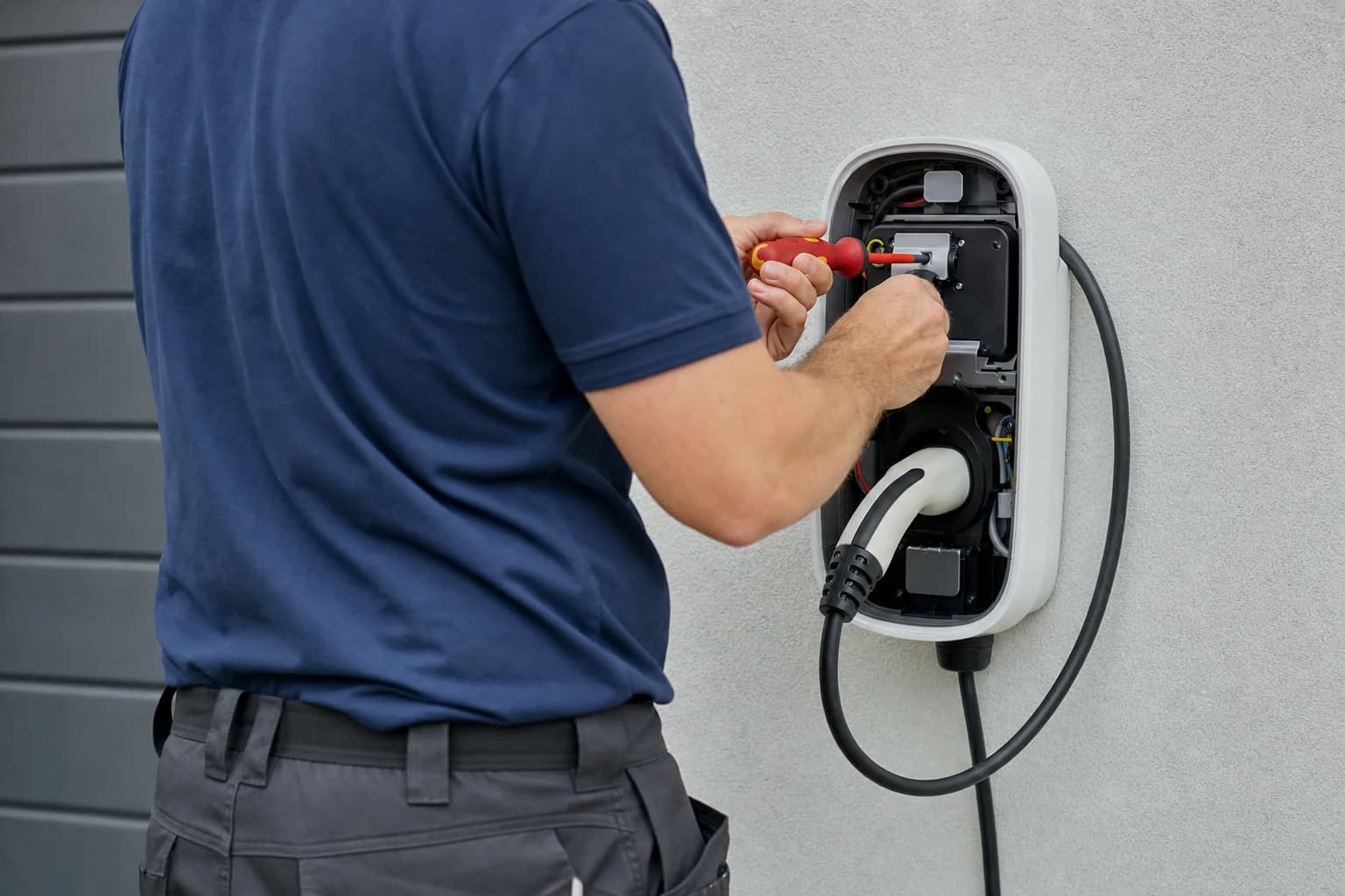 An electrician working on the faceplate of a wall mounted EV charger